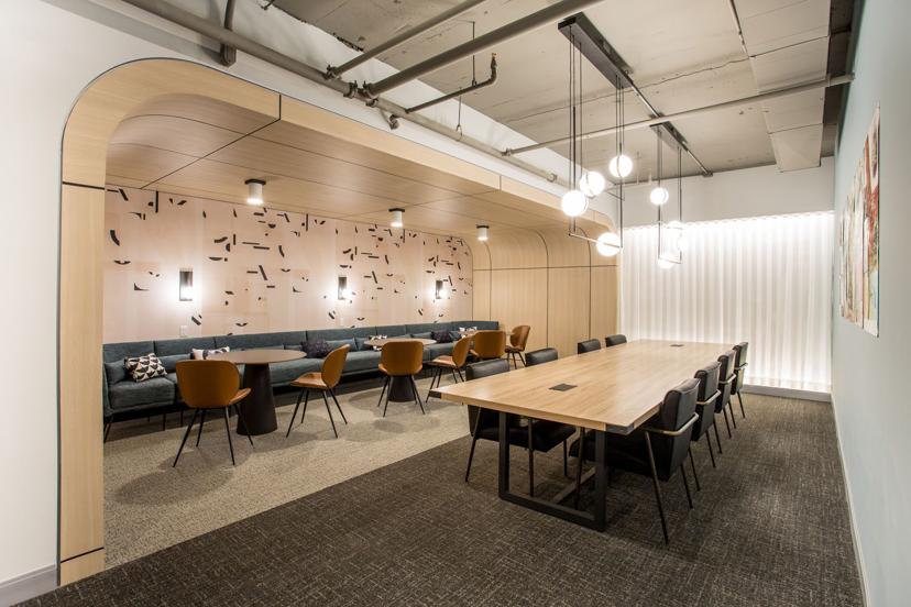 Modern conference room with a long table, black chairs, and a cozy lounge area featuring wooden decor, pendant lights, and abstract wall art.