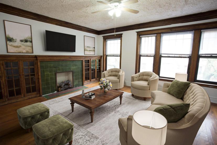 Cozy living room with beige sofas, green cushions, a wooden coffee table, floral centerpiece, a fireplace, and a ceiling fan.