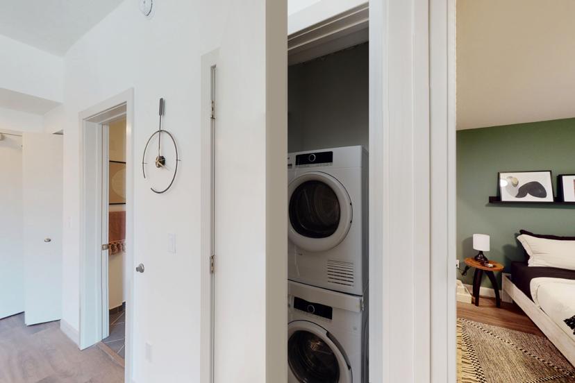 Hallway leading to a laundry closet with a stacked washer and dryer, adjacent to a bathroom and a bedroom with green walls and modern decor.