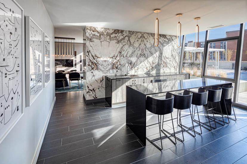 Modern kitchen with marble island, high-back stools, large windows, abstract wall art, and sleek lighting fixtures.