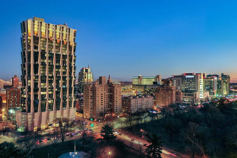 Aerial view of a cityscape at dusk, showcasing a distinctive, modern high-rise building with angled architecture amidst urban surroundings.